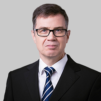 Porträt eines Mannes mit Brille und Anzug mit Krawatte vor neutralem Hintergrund