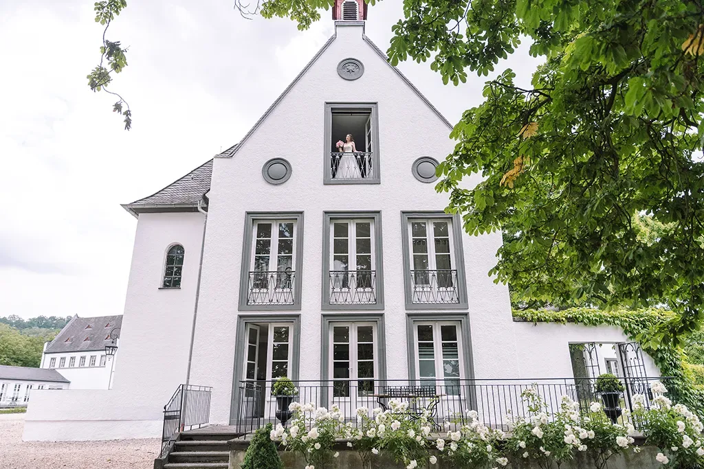 Brautpaar vor weißer Kapelle mit Blumendekoration beim Hochzeitsfotoshooting