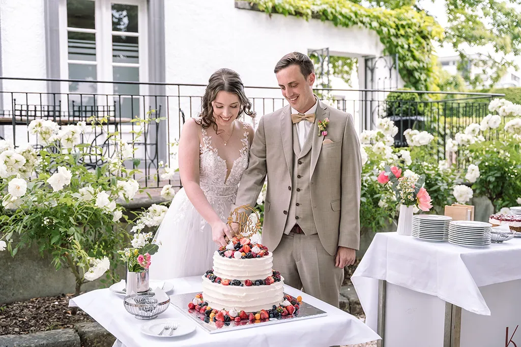 Brautpaar schneidet Hochzeitstorte auf Terrasse mit Blumendekoration