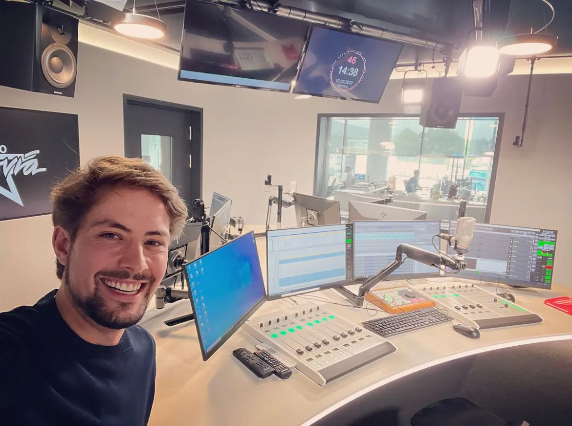 Gérôme Ehrler lächelt im Radiostudio an Schreibtisch mit Technik und Monitoren