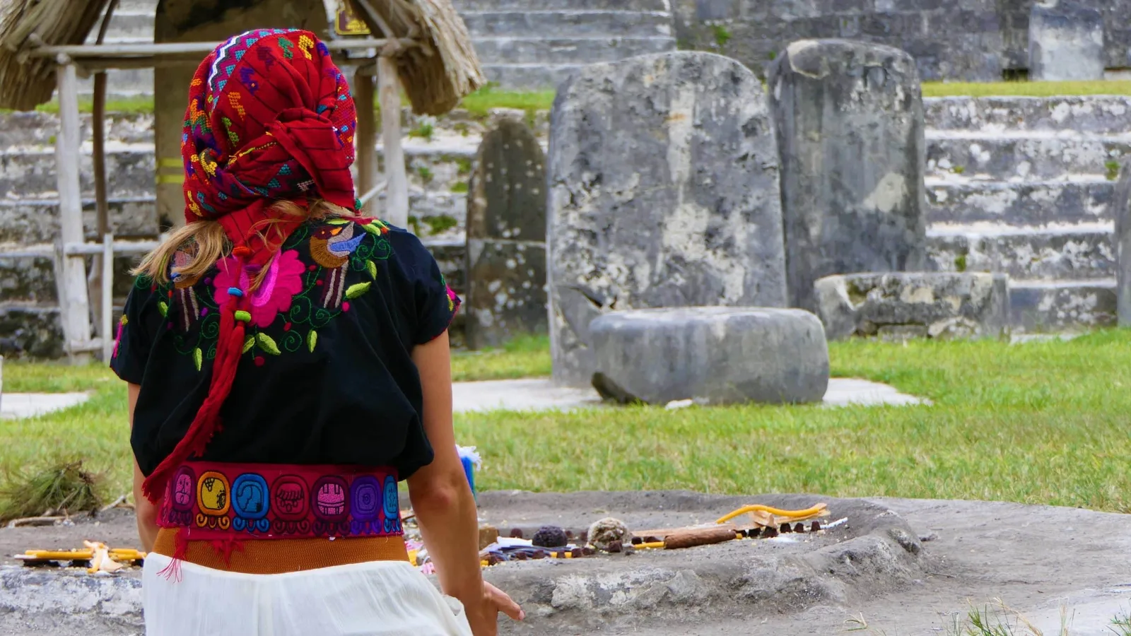 Frau in traditioneller bunter Kleidung mit rotem Kopftuch vor Maya-Ruinen