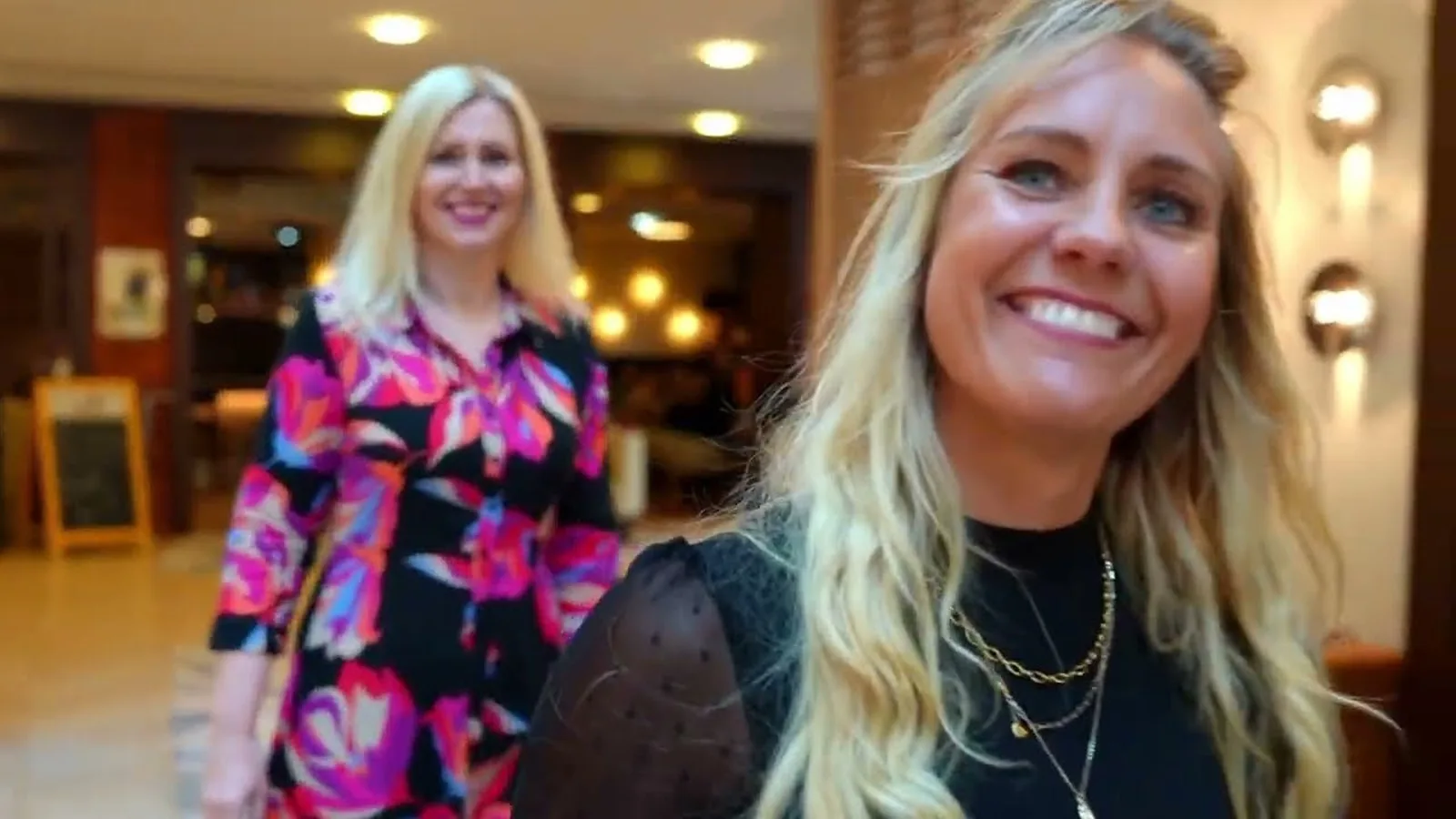 Werde zertifizierter Holistic Skin and Health Expert 3 Zwei blonde Frauen in modernem Interior, eine trägt bunte pinkfarbene Jacke, lächeln in die Kamera