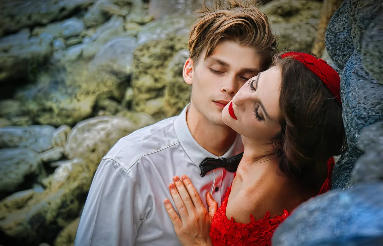 Werde zum Frauenmagnet! – Dating-Kurs für Männer von Nadine Kretz 8 Junger Mann und Frau in rotem Kleid mit rotem Haarband an Felsenwand, innige Pose