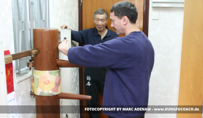 Trainer demonstriert Wing Chun Holzpuppen-Training mit Schüler in Trainingsraum