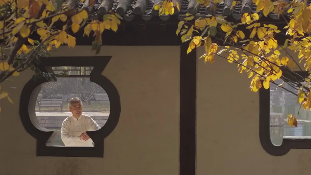 Meister praktiziert Tai Chi Bewegung in traditionellem chinesischen Garten mit runden Fenstern und Herbstlaub