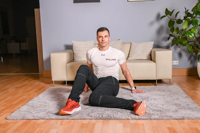 Mann sitzt auf Matte und mobilisiert Hüfte und Beine