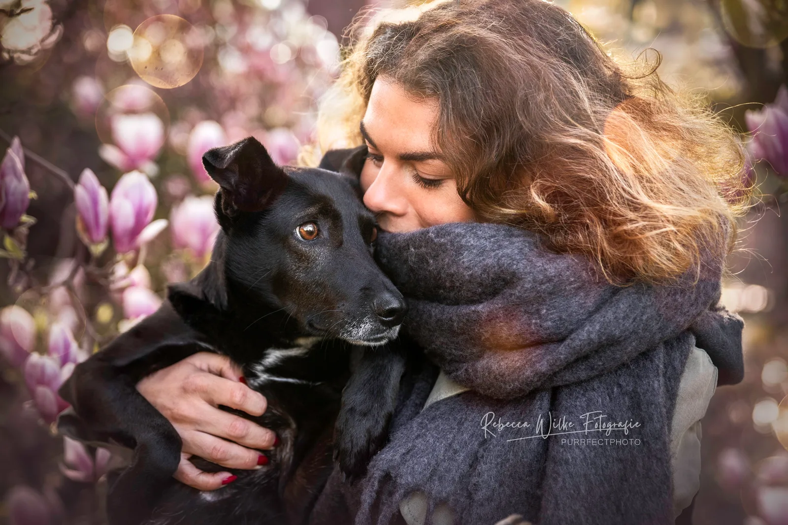 Frau mit schwarzem Hund vor unscharfen Magnolienblüten, Porträt mit warmem Licht