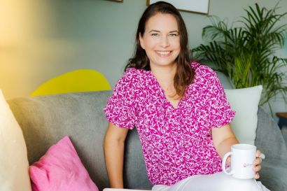 Junge Frau im rosa Blumenmuster sitzt mit Tasse auf Sofa