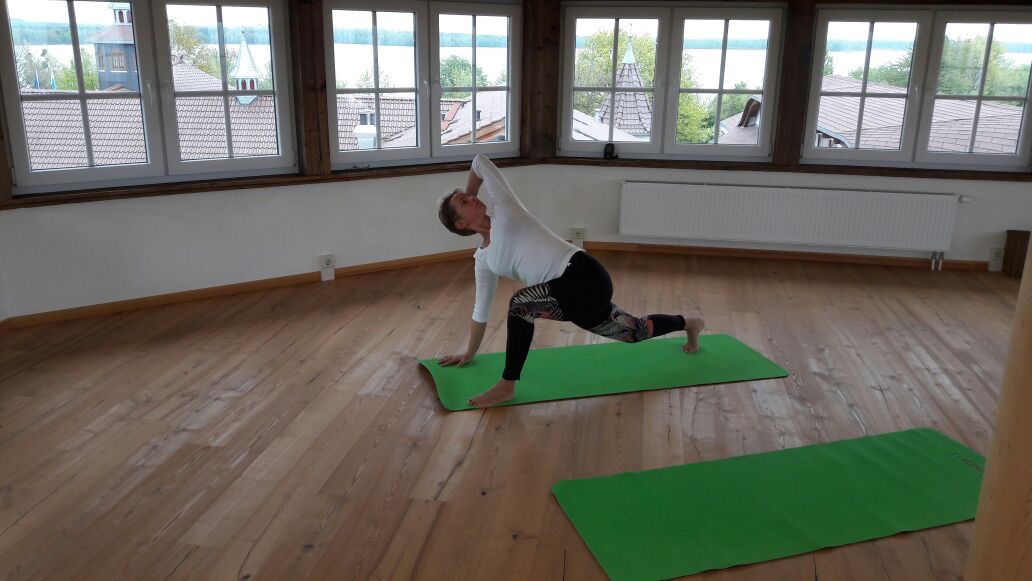 Yoga Live Online Kurs von Anke Schneider 5 Frau in Yoga-Pose auf grüner Matte in hellem Studio mit großen Fenstern