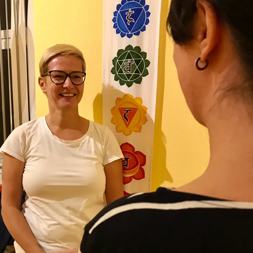 Yoga Live Online Kurs von Anke Schneider 4 Anke Schneider im Coaching-Gespräch vor gelbem Hintergrund mit Chakra-Symbolen