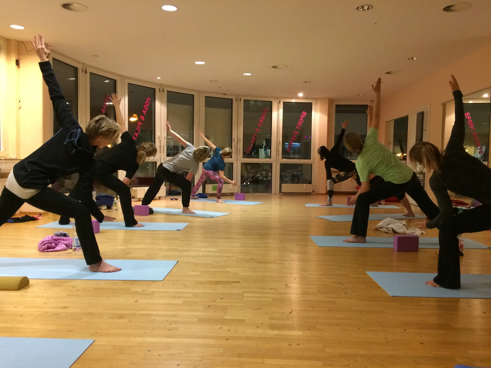 Yoga Live Online Kurs von Anke Schneider 7 Yoga-Kursgruppe in Krieger-Pose auf bunten Matten in hellem Yoga-Studio mit Spiegeln