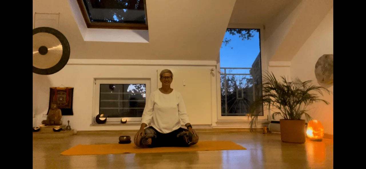 Yoga Live Online Kurs von Anke Schneider 3 Anke Schneider in Meditation auf oranger Matte in hellem Raum mit Skylight und Pflanzen