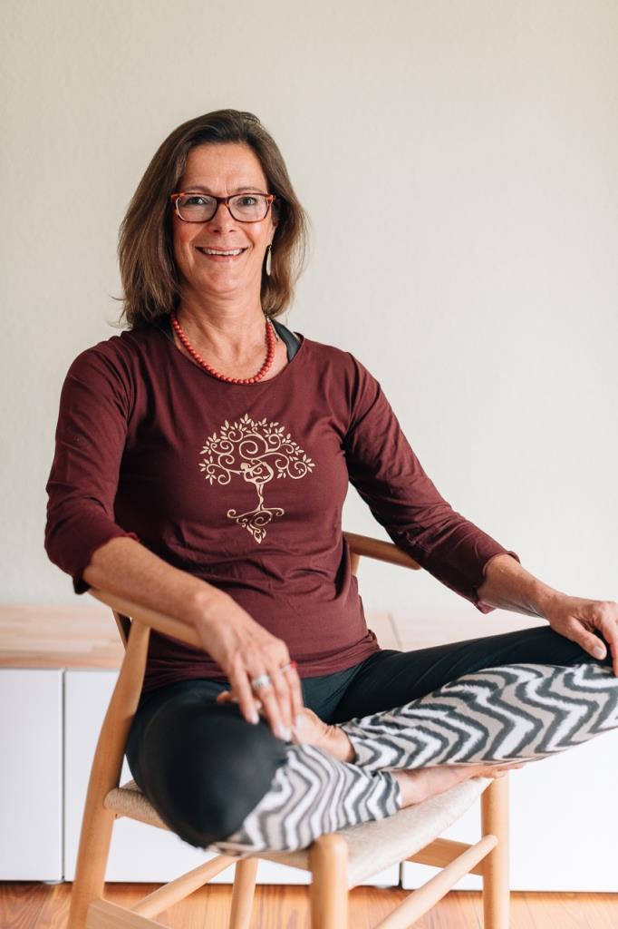 Yoga-Trainerin Gudrun Andre sitzt auf Stuhl mit Yoga-Kleidung