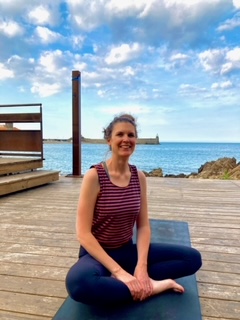 Yoga-Trainerin Julia Trabant sitzt meditierend auf Matte am Meer