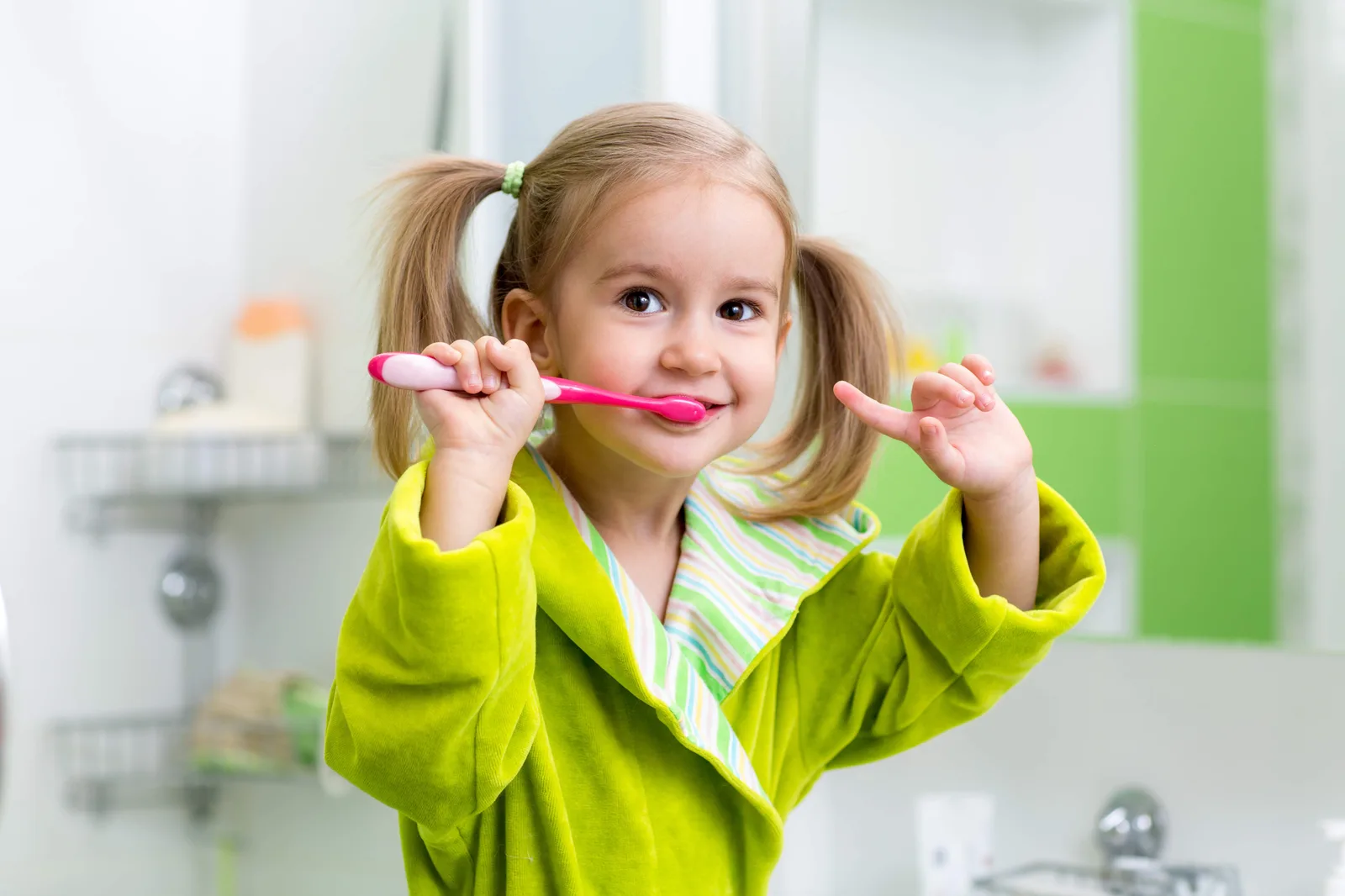 Kleines Mädchen mit Zahnbürste im Badezimmer, grüner Pulli, Pigtails, lächelnd