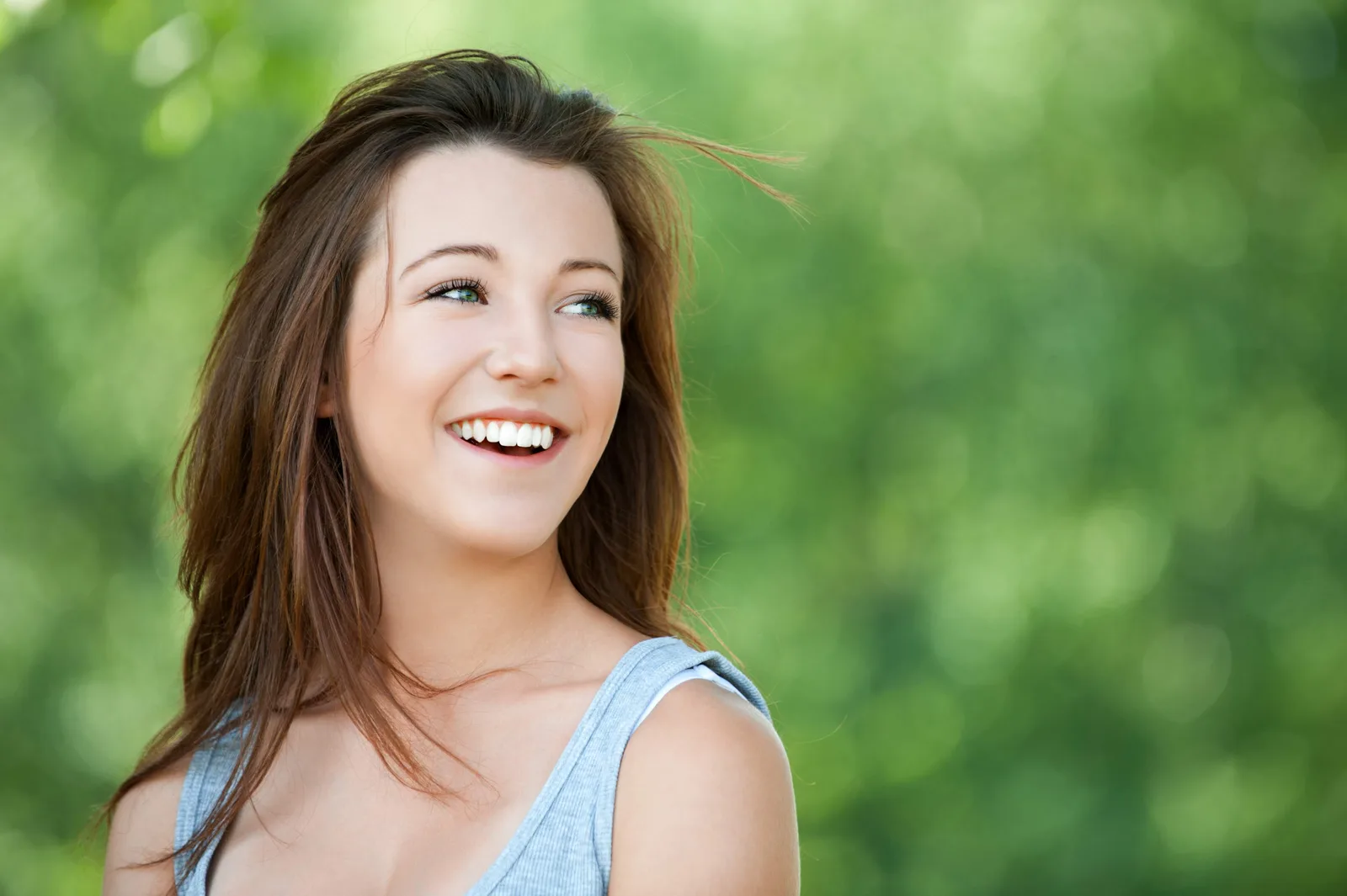 Junge Frau mit perfektem weißem Lächeln, braune Haare, grüner unscharfer Hintergrund