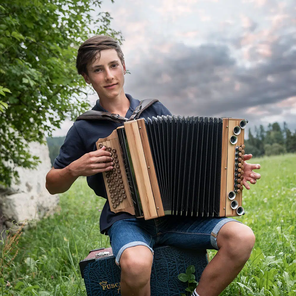 Junge mit Steirischer Harmonika im grünen Freien vor Bergen
