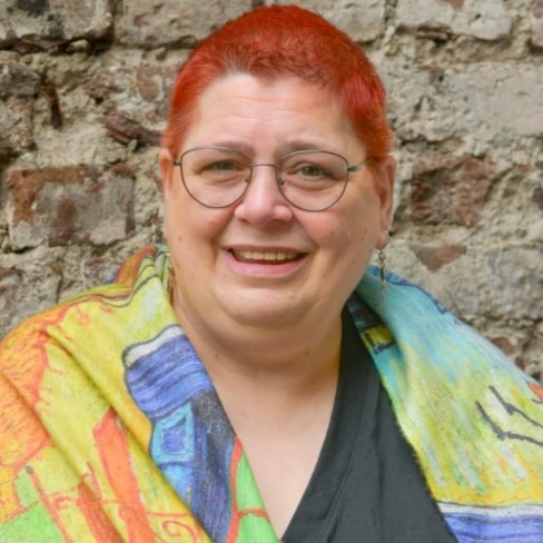 Frau mit roten Haaren und Brille, karierte Jacke, vor Steinwand
