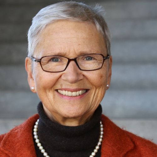 Porträtfoto von Michaela Gloeckler, Frau mit weißem Haar, Brille, rotem Pullover und Perlenkette