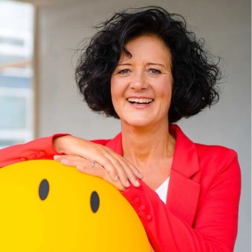 Porträtfoto von Susanne Klaus, Frau mit schwarzem Haar, rotem Blazer neben gelbem Objekt