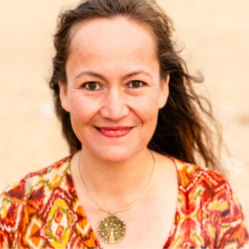 Porträtfoto von Anna Nyugen, Frau mit braunem Haar, buntem Pullover vor hellem Hintergrund