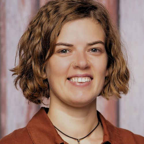 Katharina Sonnberger, blonde Frau mit graublauem Shirt vor grünem Naturhintergrund