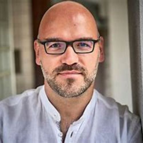 Fabian Strumpf, junger Mann mit braunen Haaren und Halsband vor rostrotem Hintergrund