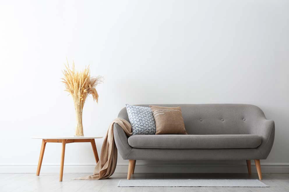 Modernes Wohnzimmer mit grauem Sofa, Holztisch, Trockenblumen und minimalistischem Design