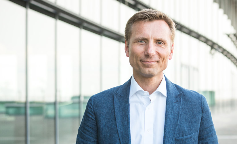 René Penselin Porträt in blauem Blazer vor modernem Architektur-Hintergrund mit Metallstreben