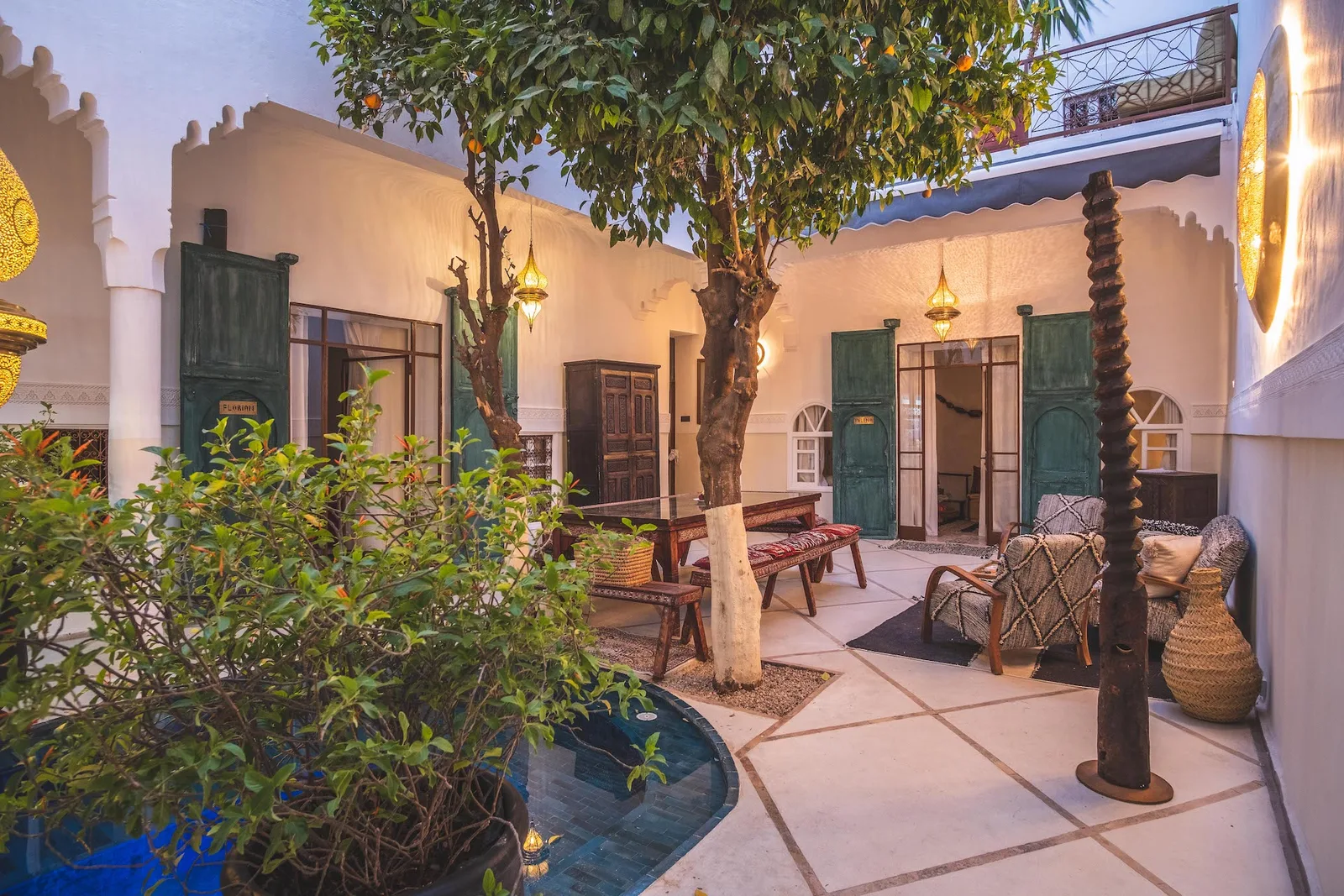 Marokkanischer Riad-Innenhof bei Dämmerung mit weißen Mauern, grünen Türen und traditionellen Laternen