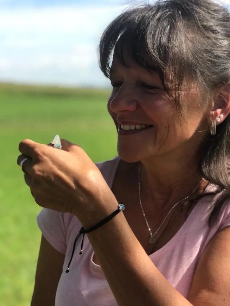 Petra Biegert in rosa Top lächelt auf grüner Wiese mit Schmetterling auf ihrer Hand