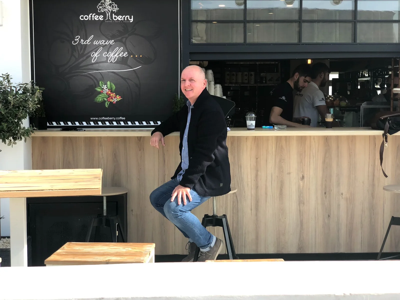 Torsten Jaeger sitzt in einem modernen Café mit der Aufschrift Coffee Berry, trägt schwarze Jacke und hellblaues Hemd