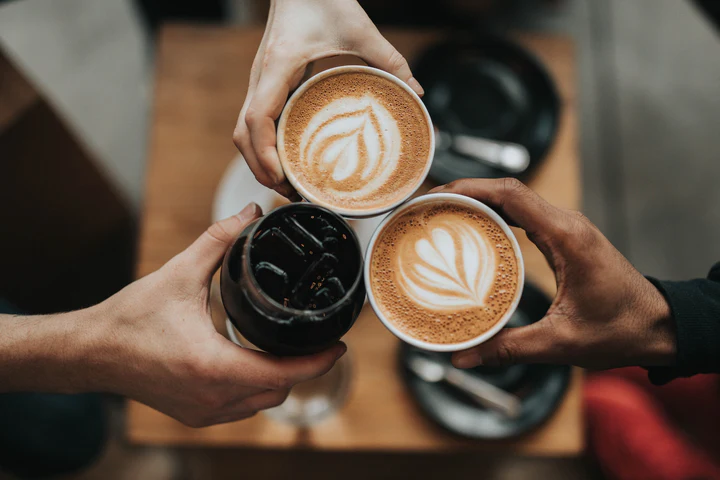 Zwei Hände halten drei Cappuccino-Tassen mit Latte-Art zusammen