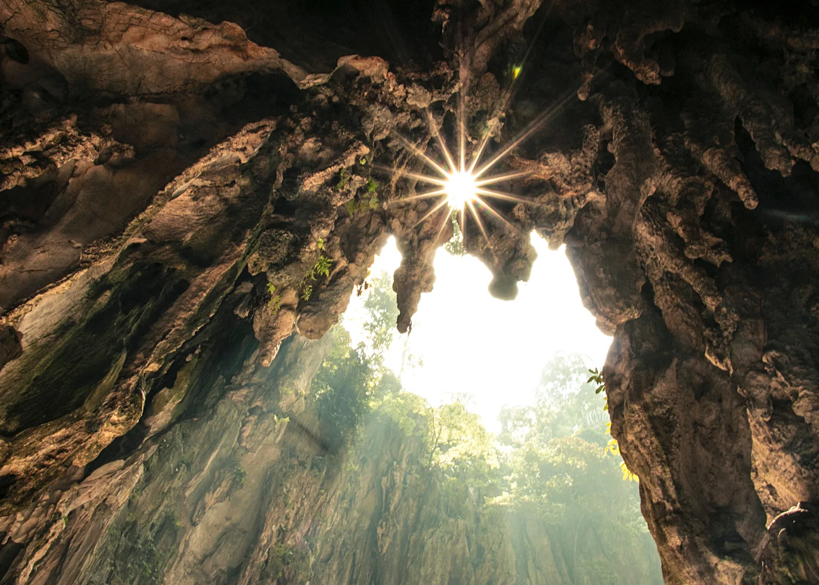 Höhle mit Lichteinfall von oben, Strahlen durchbrechen Dunkelheit, symbolisiert Übergang und Erleuchtung