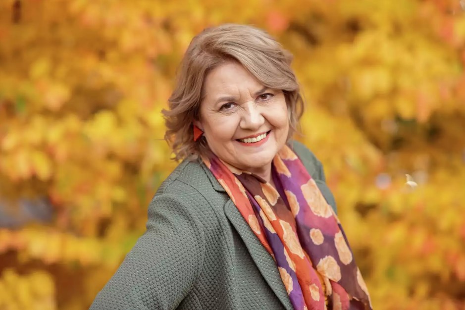 Portrait einer Frau mittleren Alters mit grauem Haar vor Herbstlaub-Hintergrund