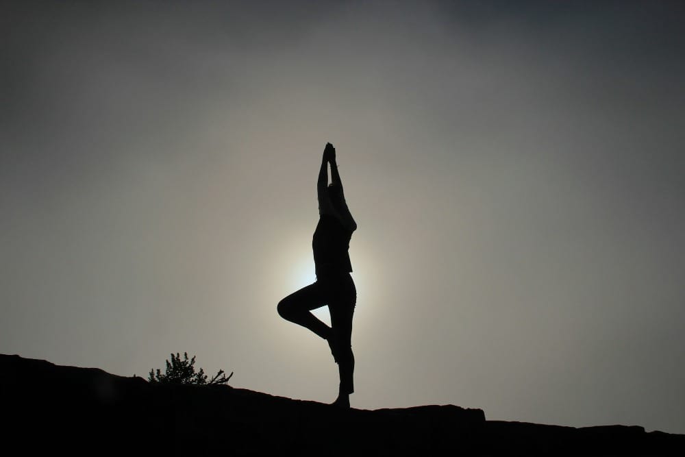 Silhouette einer Frau in Yoga-Pose (Vrschikasana) gegen Himmel auf Felsen, 30-Tage-Yoga-Kurs yippy®