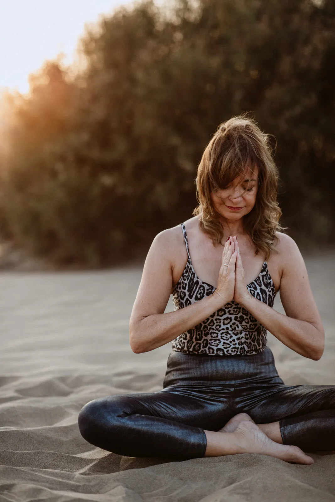 Frau mit geschlossenen Augen sitzt meditierend am Strand in Lotus-Position mit Namaste-Geste