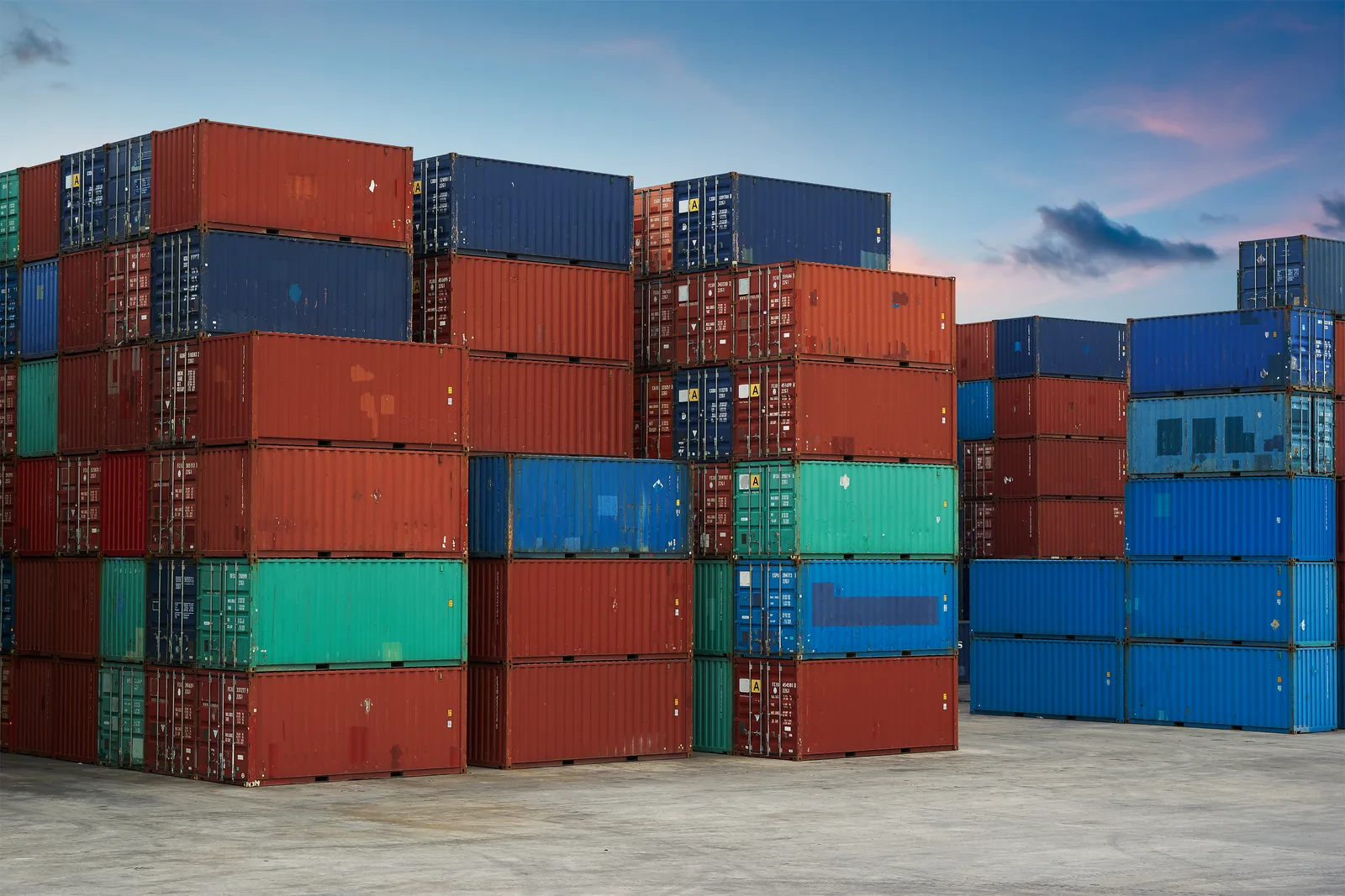Gestapelte farbige Frachtcontainer am Hafen bei Sonnenuntergang, rot, blau und grün