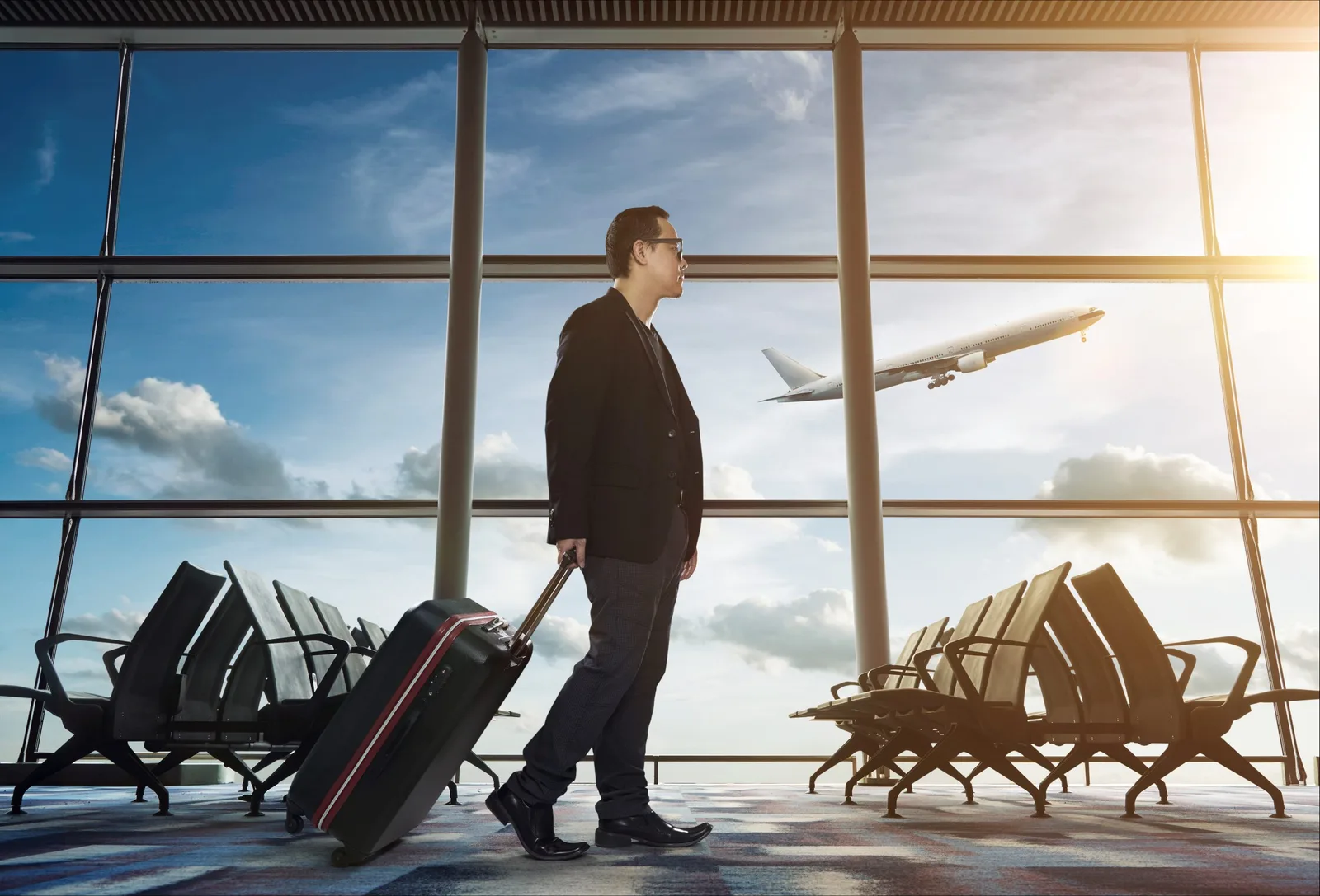 Geschäftsmann mit Koffer im Flughafen-Terminal, Blick auf startenden Flugzeug durch große Fenster