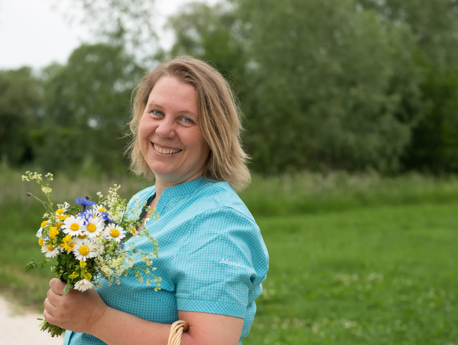 Heike Engel hält Wildblumenstrauß im hellblauen Hemd