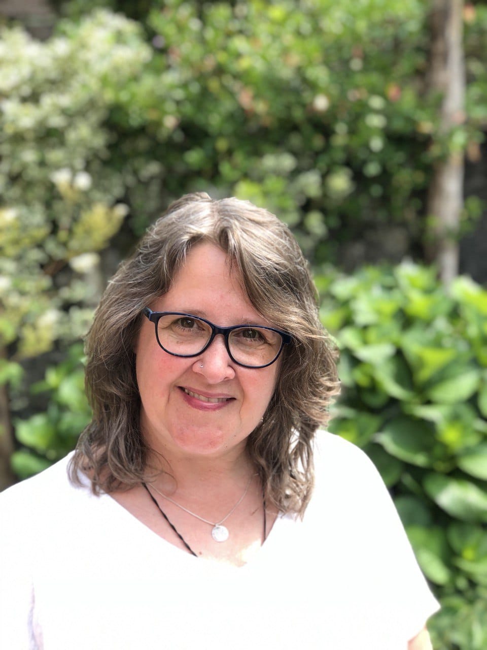 Tanja Francisco, Frau mit Brille und braunem Haar vor grünem Garten-Hintergrund lächelnd