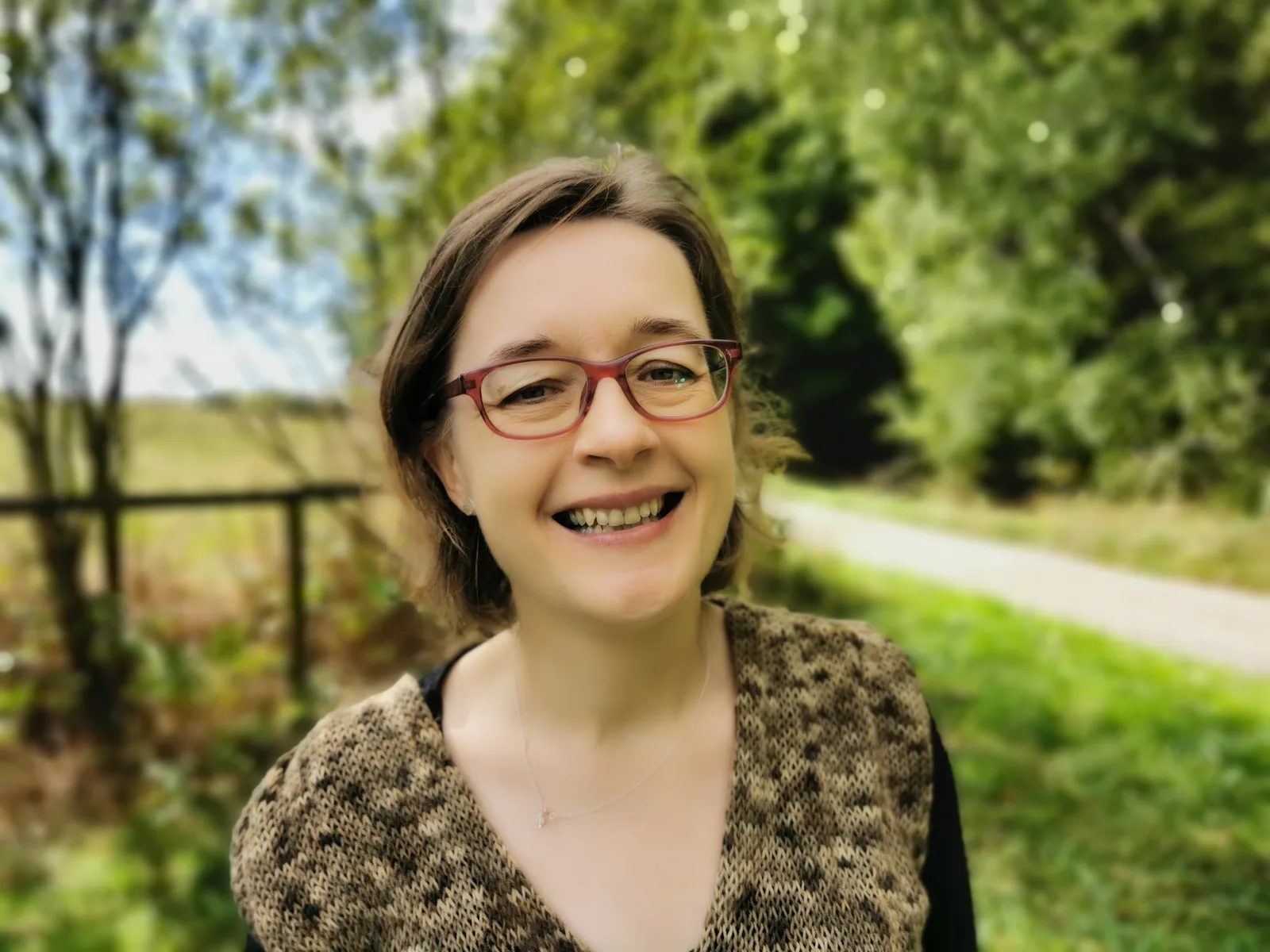 Katharina Kriegelsteiner, junge Frau mit Brille und braunem Haar vor grüner Naturkulisse lächelnd