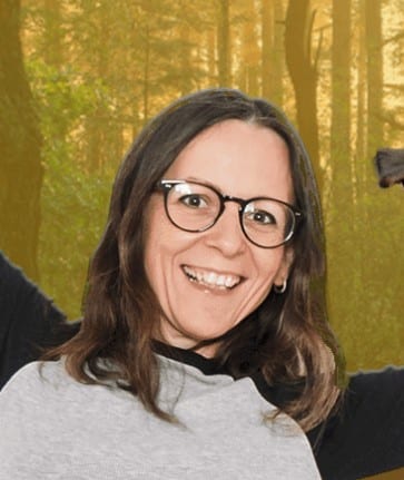 Anita Zoder, junge Frau mit Brille und braunem Haar vor gelblichem Hintergrund lächelnd