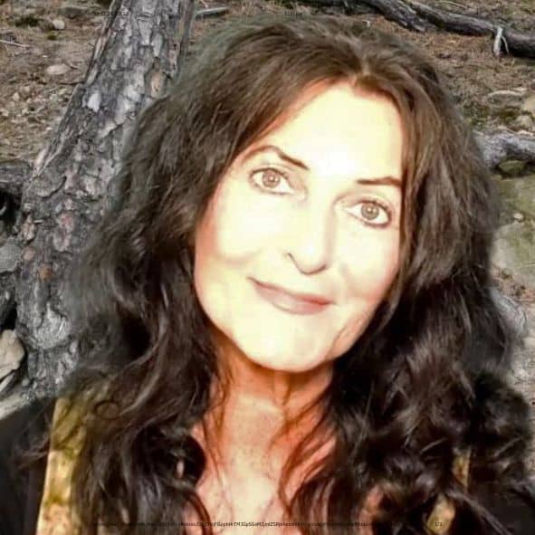 Britta Diana Petri, Frau mit braunem Haar vor Baumstamm im Wald lächelnd