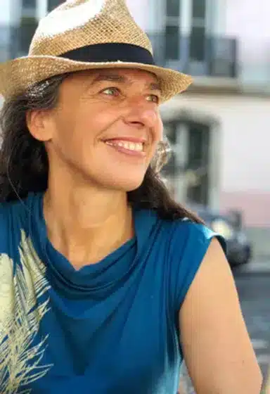 Frau mit Strohhut und blauem Top, lächelnd, urbaner Hintergrund