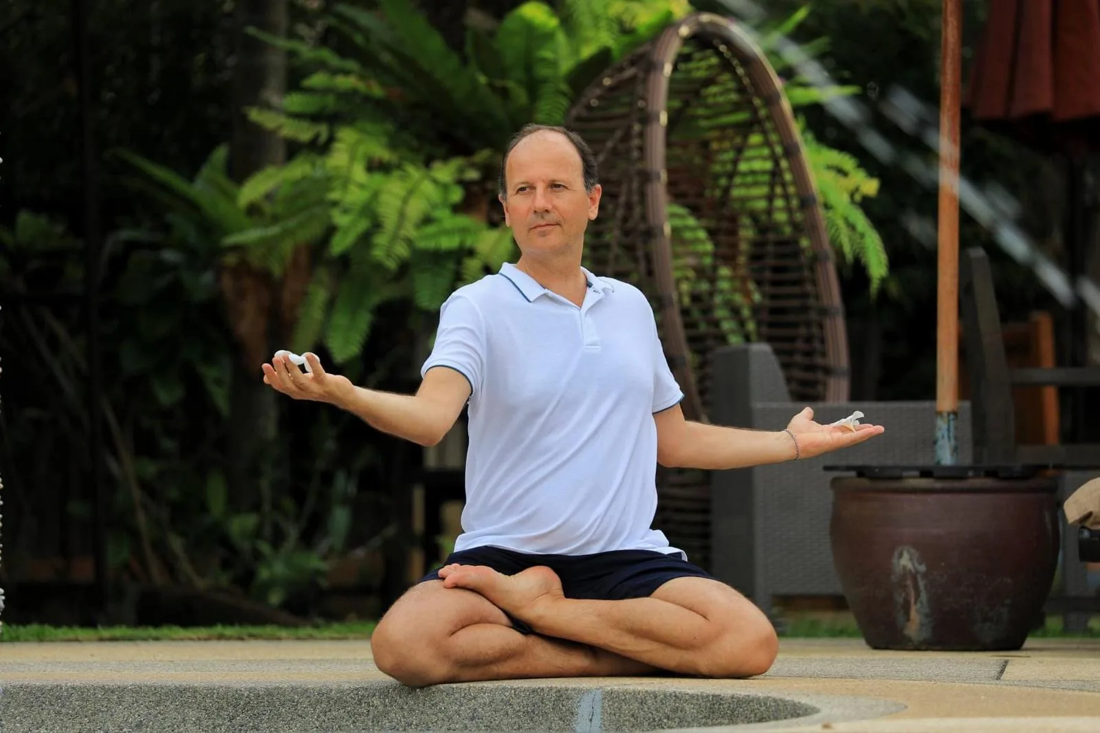 Remo Rittiner im Garten vor Hecke, weiß-blaues Polo-Shirt, Hände in Mudra-Position