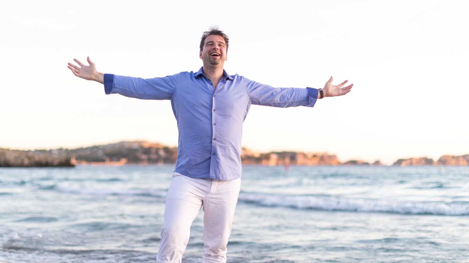 Björn Heede lächelnd am Strand mit ausgebreiteten Armen, Porträt