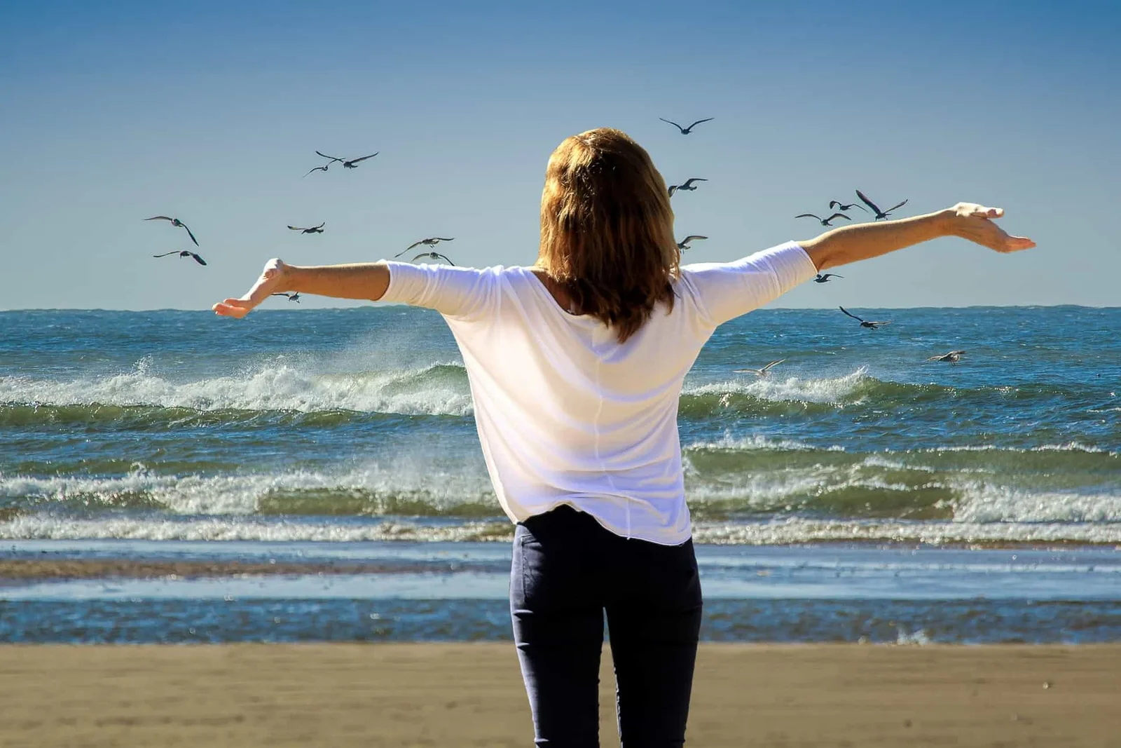 Frau von hinten am Strand mit ausgestreckten Armen, Meereslandschaft, Vögel, Freiheit