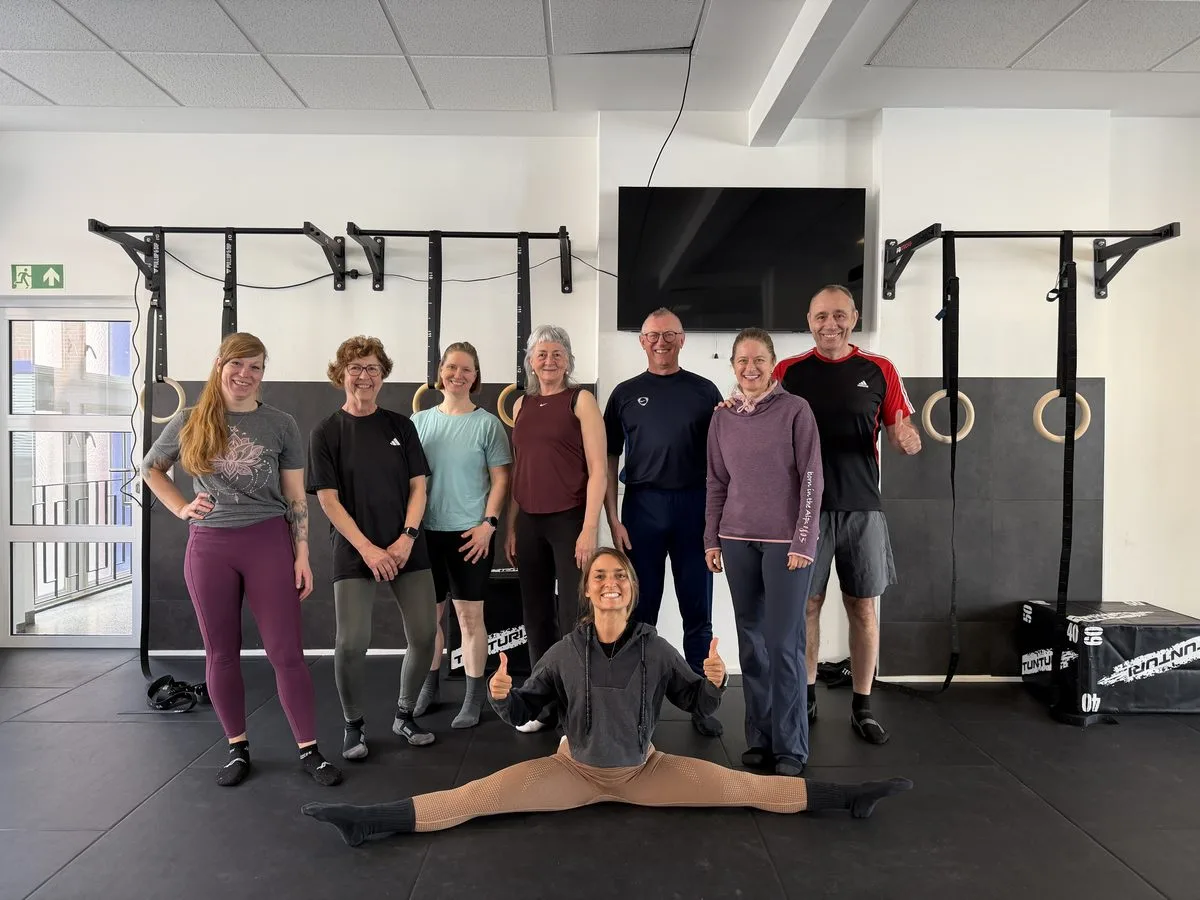 Gruppenfoto von neun Personen verschiedenen Alters in Fitness-Studio mit Pull-up-Stangen