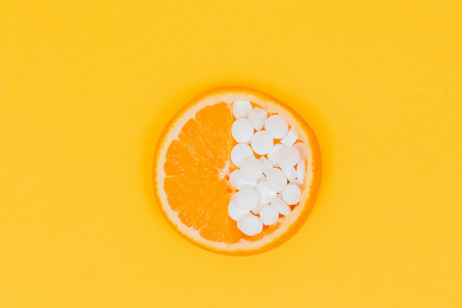 Orange Frucht auf gelbem Hintergrund, zur Hälfte mit weißen Kapseln gefüllt